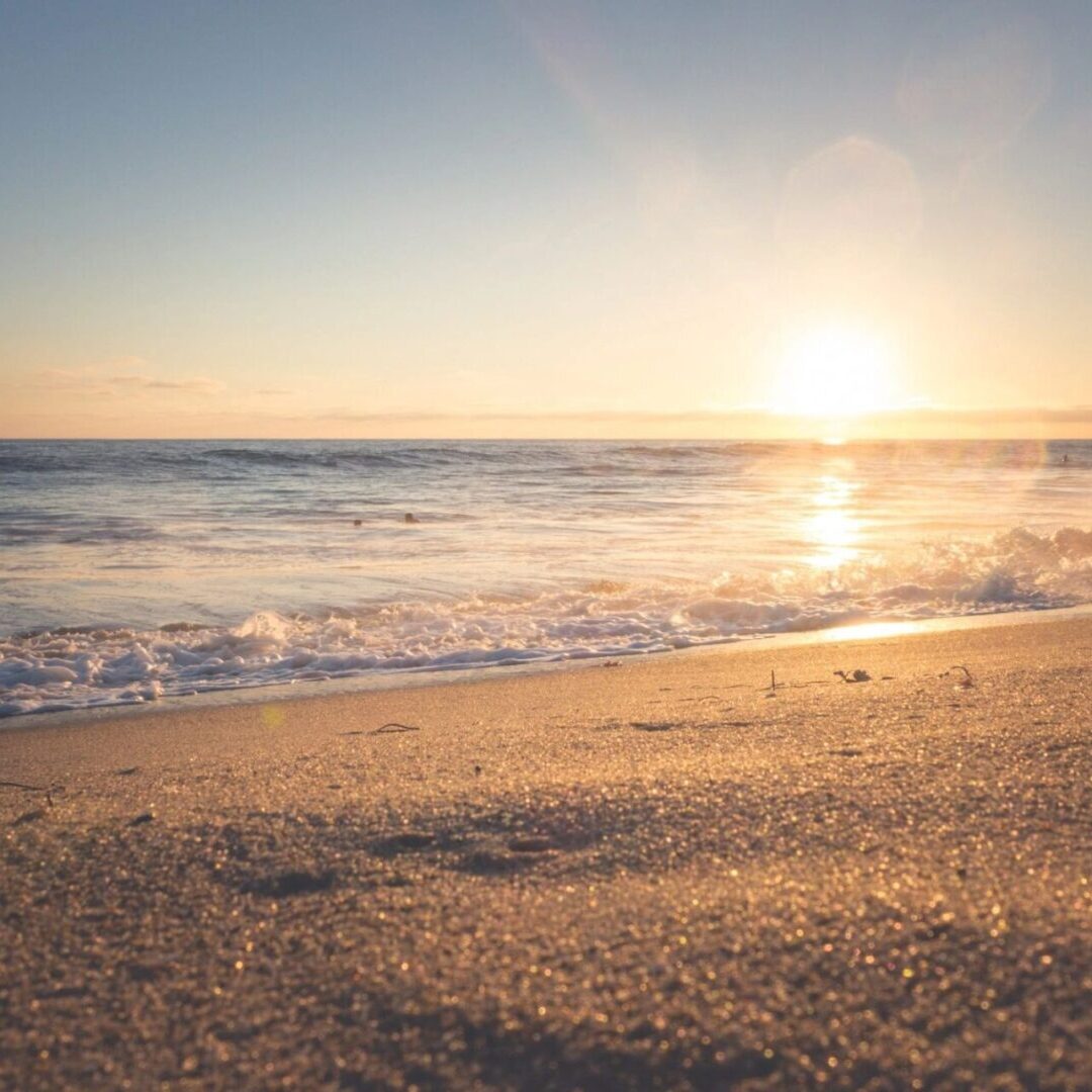 A beach with the sun setting in the background.